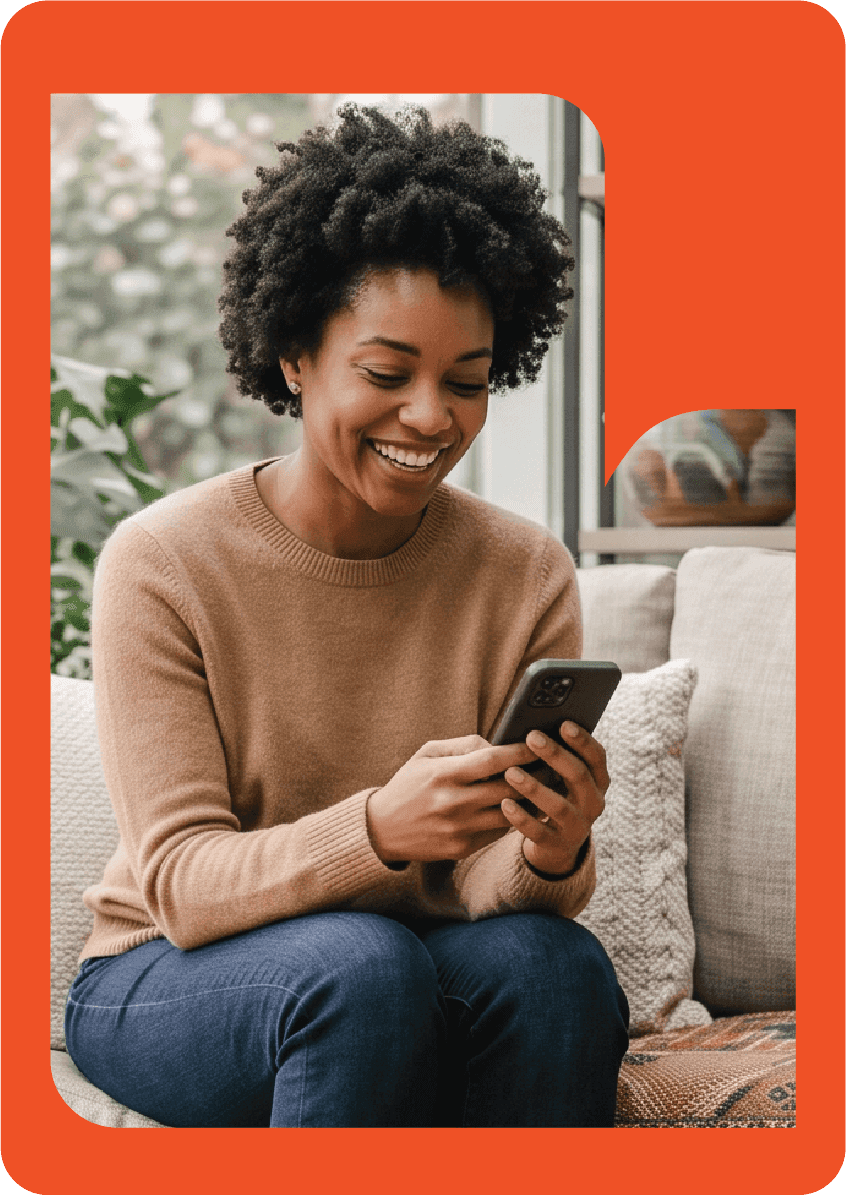 Une personne assise sur un canapé chez elle sourit en utilisant son téléphone
